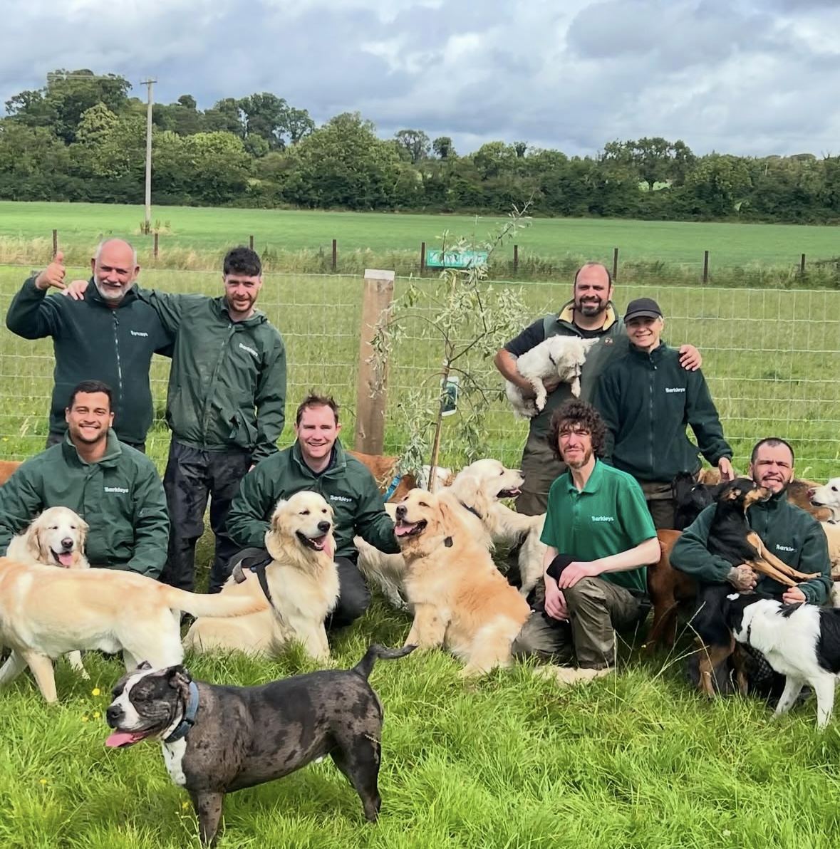 The whole Barkleys team in their green fleeces with the pack of dogs at the farm
